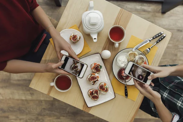 Vue de dessus des personnes utilisant des smartphones et photographier des hors-d'œuvre pendant le petit déjeuner — Photo de stock