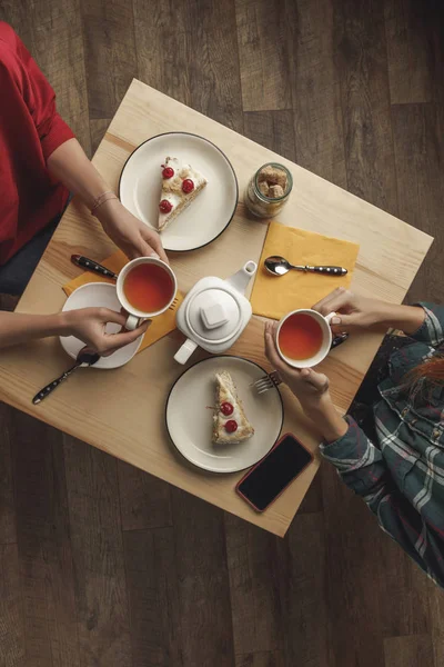 Ansicht von zwei Personen, die Tee über dem Tisch mit Gebäck und Smartphone trinken — Stockfoto