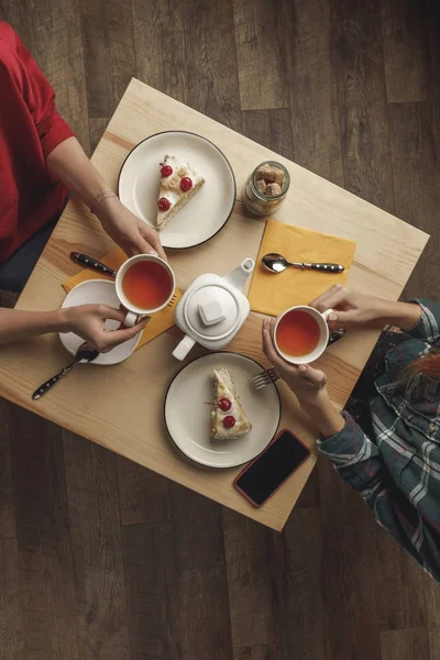 Ansicht von zwei Personen, die Tee über dem Tisch mit Gebäck und Smartphone trinken — Stockfoto