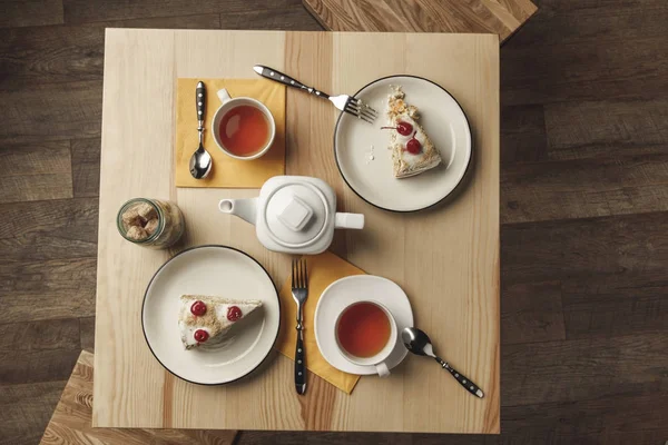 Вид зверху на чайник, дві чашки з гарячим чаєм і смачною випічкою на столі — стокове фото