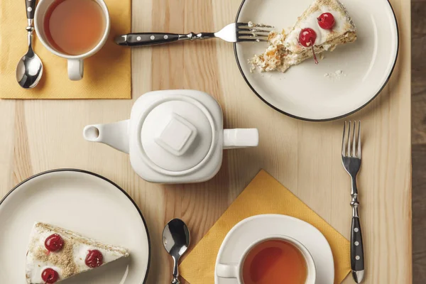 Vista superior do bule, duas xícaras com chá quente e deliciosos bolos em pratos — Fotografia de Stock