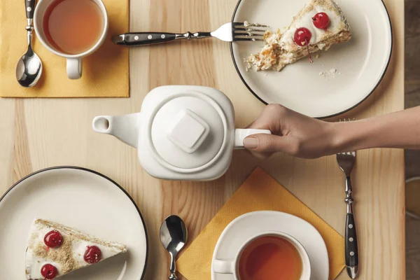 Top view of person holding teapot and tea set with pastries on table — Stock Photo