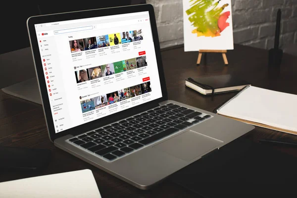 Close-up view of designer workplace with notebooks and laptop with youtube website on screen — Stock Photo