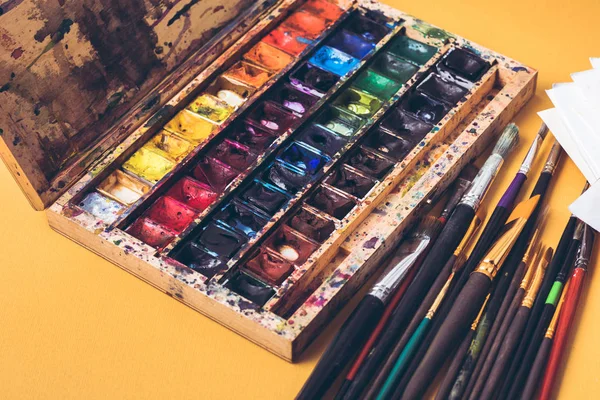 Nahaufnahme der chaotischen Schachtel mit Aquarellfarben und Pinseln am Designerarbeitsplatz — Stockfoto