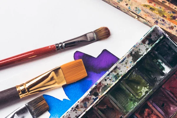 Close-up view of watercolor paints and paintbrushes with drawing album at designer workplace — Stock Photo