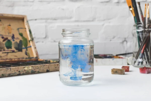 Nahaufnahme eines Glasgefäßes mit Wasser und blauer Farbe am Designerarbeitsplatz — Stockfoto