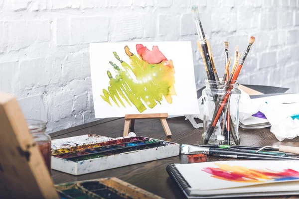 Close-up view of abstract sketches, watercolor paints and paintbrushes at designer workplace — Stock Photo