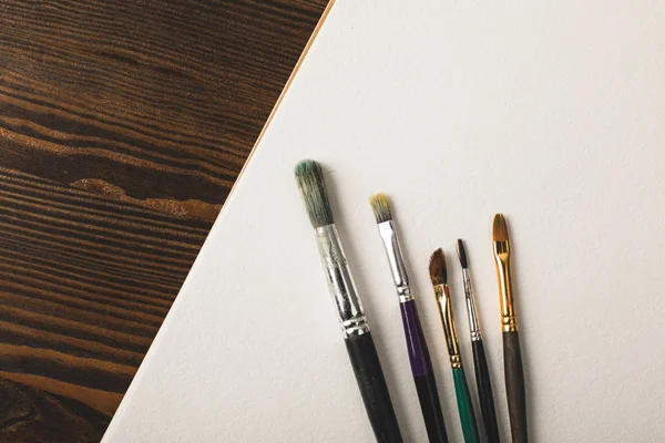 Top view of paint brushes and blank drawing album on wooden table — Stock Photo