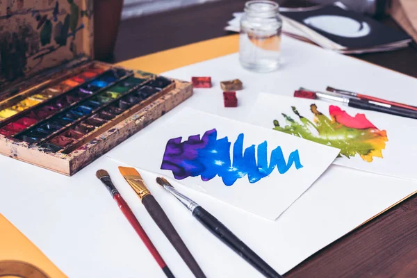 Nahaufnahme von Aquarellfarben, Pinseln und abstrakten Skizzen am Designerarbeitsplatz — Stockfoto
