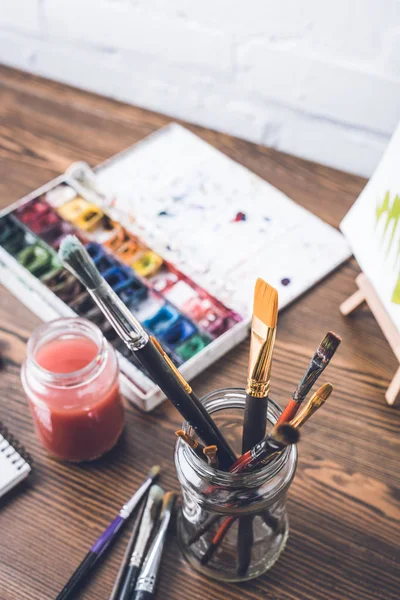 Foyer sélectif des peintures à l'aquarelle et des pinceaux sur le lieu de travail du concepteur — Photo de stock