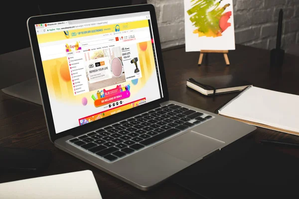 Close-up view of designer workplace with notebooks and laptop with aliexpress website on screen — Stock Photo