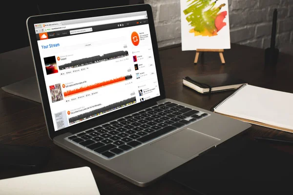 Close-up view of designer workplace with notebooks and laptop with soundcloud website on screen — Stock Photo