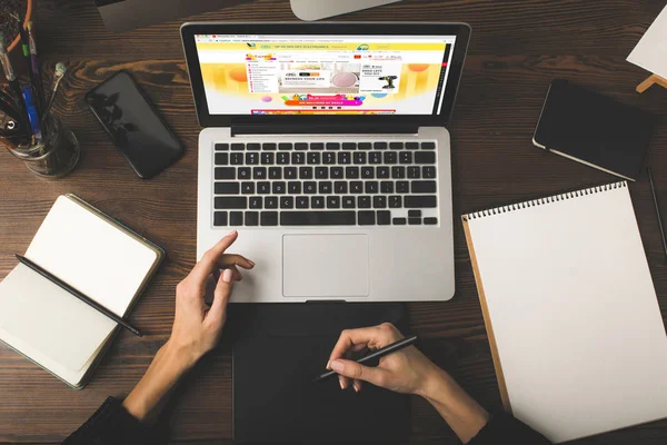 Schnappschuss eines Designers mit Grafik-Tablet und Laptop mit aliexpress-Website auf dem Bildschirm — Stockfoto