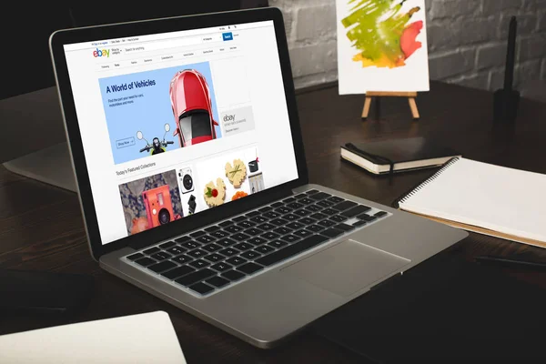 Lugar de trabajo del diseñador con el ordenador portátil y el sitio web ebay en pantalla - foto de stock