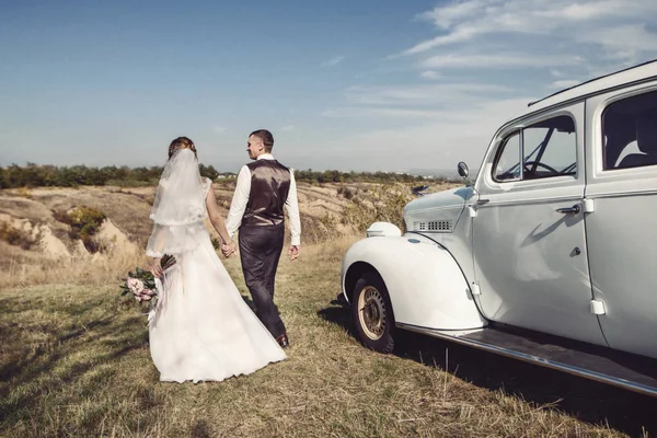 Prachtige bruid en bruidegom plezier met retro auto in de natuur — Stockfoto