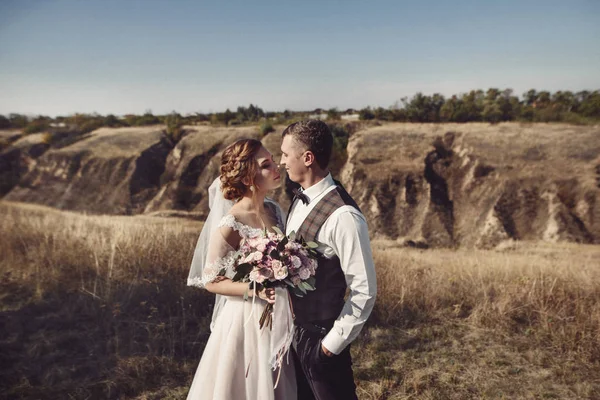 花と緑の花束と結婚式の服装でのカップルは庭の背景に手アット サンセット、花嫁と花婿 — ストック写真