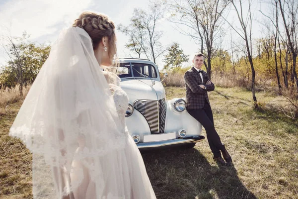 Gelukkige bruid en bruidegom knuffelen en poseren in de buurt van oude retro auto befo — Stockfoto