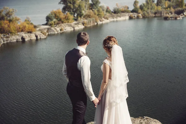 Schönes Hochzeitspaar küsst und umarmt sich am Ufer eines Gebirgsflusses mit Steinen — Stockfoto