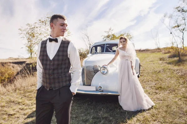 Πανέμορφη νύφη και ο γαμπρός διασκεδάζοντας με ρετρό αυτοκίνητο στη φύση — Φωτογραφία Αρχείου
