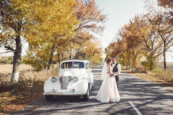 Щаслива наречена і наречена обіймаються перед старовинним автомобілем — стокове фото