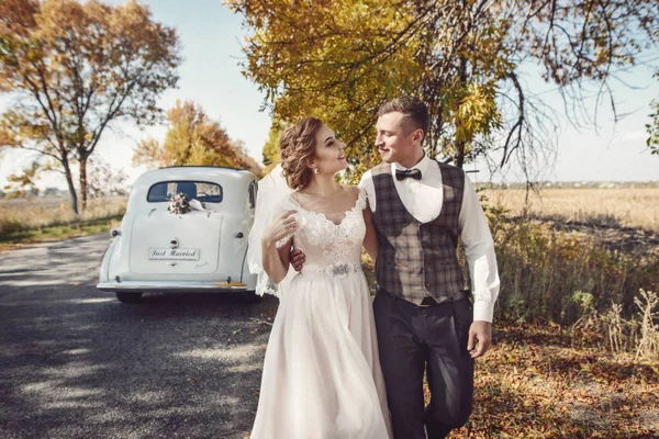 Νύφη και γαμπρός αγκαλιές στο μπροστινό μέρος του αυτοκινήτου παλιά — Φωτογραφία Αρχείου