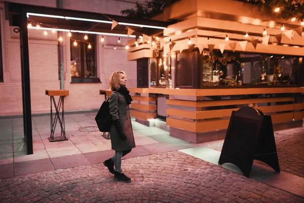 Chica en un abrigo y bufanda va al lado de la cafetería en la víspera — Foto de Stock