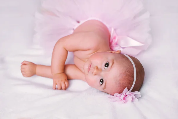 Pasgeboren babymeisje dragen een witte haakwerk kroon, ballerina tutu, en ballet slippers. ze slaapt op roze roze lint stof. — Stockfoto