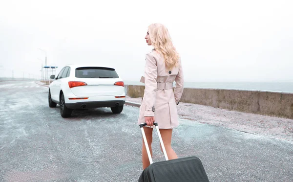 Mujer de negocios con maleta cerca del coche. De pie en el camino de fondo — Foto de Stock