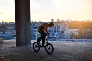 Bmx bisiklet üzerinde gökyüzü karşı Evin çatısı günbatımında atlama bir adam silüeti.