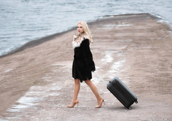 Winter travel. Portrait of a beautiful woman with suitcase near sea