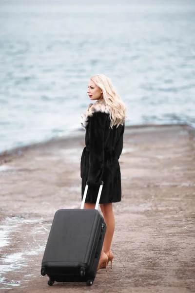 Vrouw in een full-length bontjas met een koffer, reizen en recreatie, toerisme. Meisje en een koffer. Prachtige vrouwelijke toerist met reizen koffer — Stockfoto