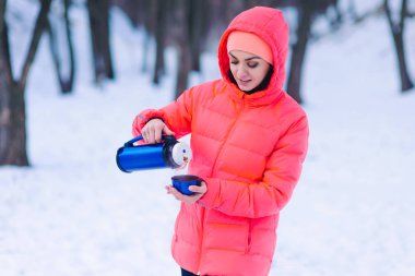kadın kırmızı ceketli bir termos çaydan ormanda kışın dökülen. tatil ve hafta sonları kış