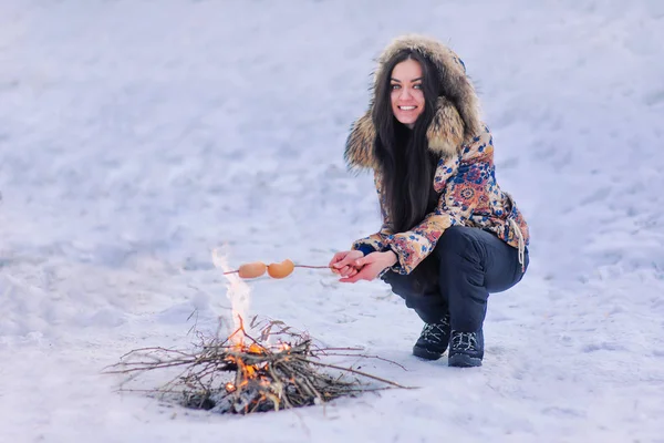 woman near the fire fry sausages in the woods in winter. tasty food