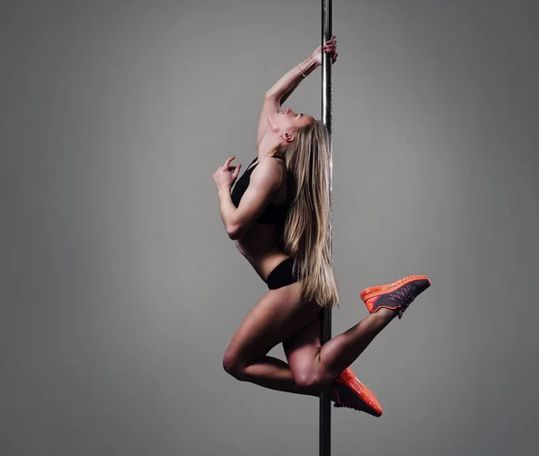 Attractive pole dancer with body-art hangs on a pylon in the studio on the dark background with a cloud of a smoke. She holds the pylon with the hands from the back and looks to the side. Verical.