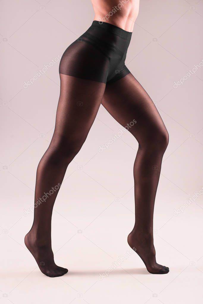 female legs in black nylon pantyhose on gray background