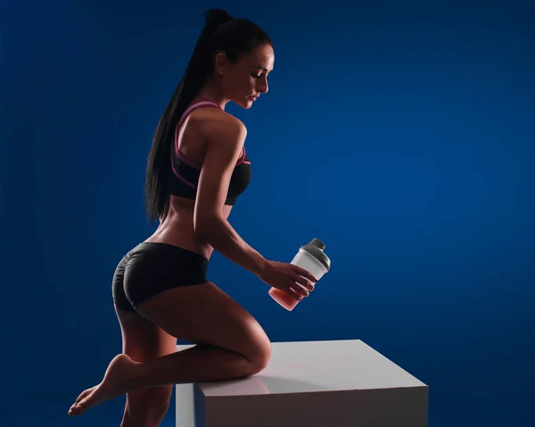 Retrato de una mujer sosteniendo un agitador de proteínas y de pie contra un fondo azul aislado . — Foto de Stock