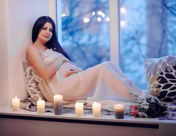自宅の窓辺に座っている若い美しい妊娠中の女性 — ストック写真