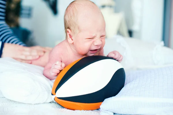 Retrato de um bebé recém-nascido de duas semanas. Ele é posado com um futebol americano — Fotografia de Stock