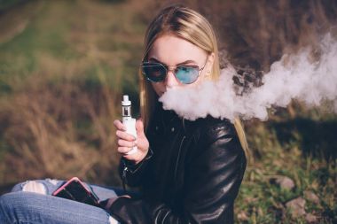 sarışın kız vaping açık havada. e-sıvı veya e-suyu Buharlaştırıcı aygıt veya e-çiğ ile kadın modeli yasaktır Meyve aromalı. Sigara içenler için modern aracı