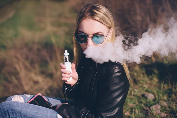 Blond meisje vaping buitenshuis. vrouwelijke model roken vruchten smaak e-liquid of e-juice met vaporisator apparaat of e-cig. Moderne gadget voor rokers — Stockfoto