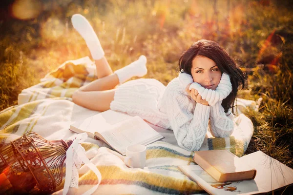 Молода красива жінка в в'язаному светрі читає книгу і бреше на плетеному восени — стокове фото