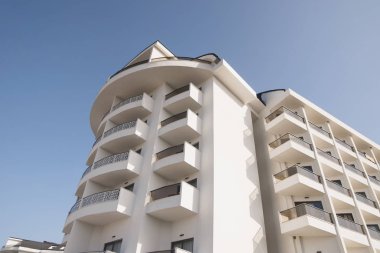 Beyaz renk otel cephe korkuluk ve mavi gökyüzü altında büyük pencereler ile beyaz altıgen otel dış düşük açılı görünüş