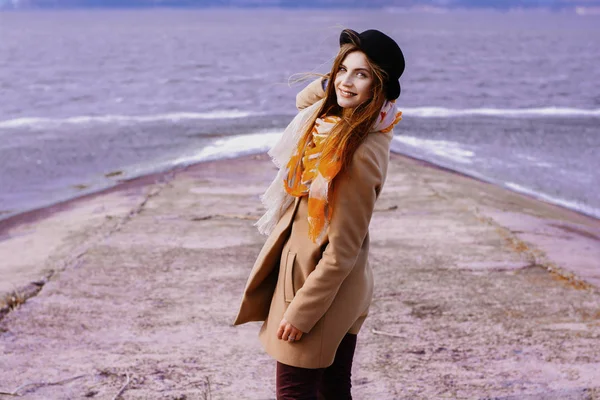 Chica pelirroja con labios rojos con un sombrero negro con el pelo largo de pie cerca del mar de invierno — Foto de Stock