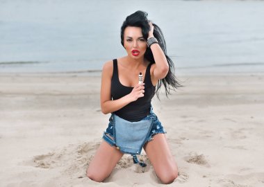 Modern e-cig mermiyi tutuyor ve yaz kum mavi deniz kenarında oturan seksi genç kız. Sigara nikotin çıkın. Genç sigara içen kadın ile elektronik sigara becerikli alet