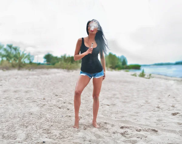 Morena chica fumando cigarrillo electrónico en la playa —  Fotos de Stock