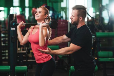 Genç bir kadın bir spor salonunda dışarı çalışırken bir halter kaldırma yardımcı antrenör