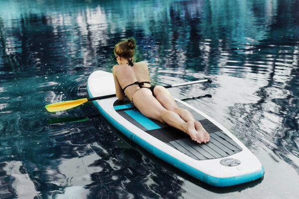 Sexy beautiful woman relaxing on a SUP board. Back view. The girl sunbathes