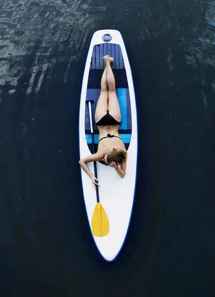 Attractive woman in bikini is sunbathing on a surfboard, aerial view — Stock Photo, Image