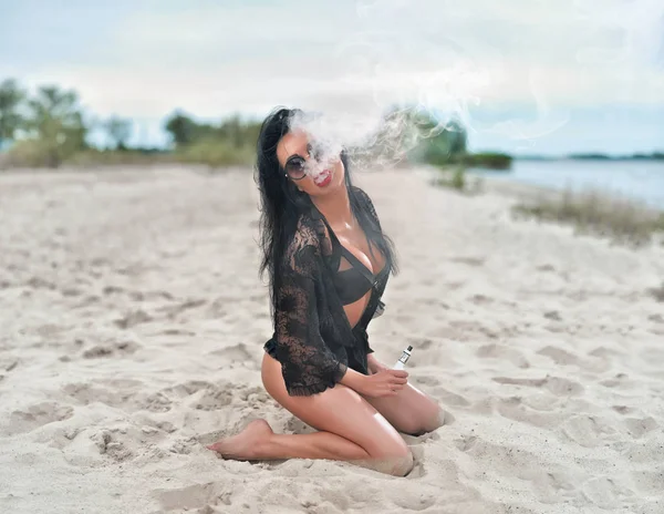 Brunette girl smoking electronic cigarette on the beach — Stock Photo, Image