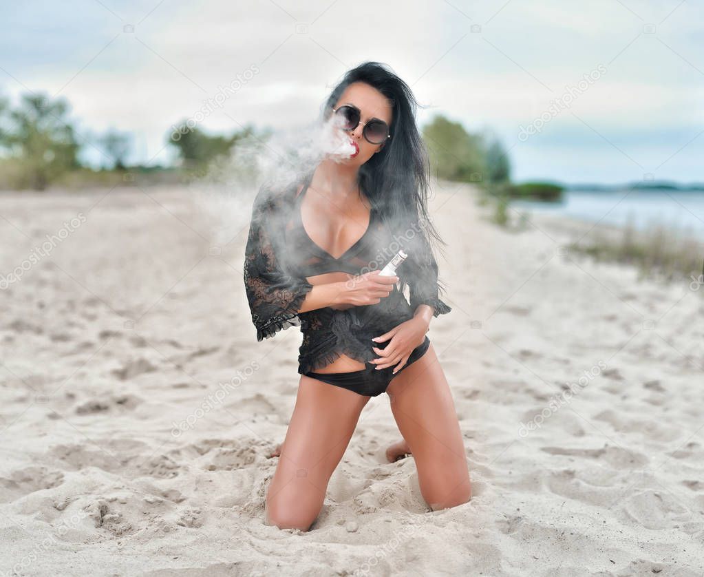 sexy young vaping girl in black Lingerie. Girl blowing vape. Vapor concept. Vaping on the beach